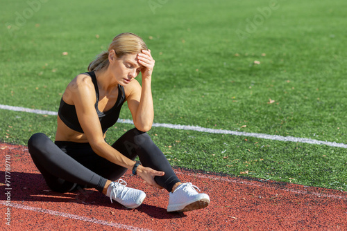 Photography Tired female athlete in sportswear sitting on a running track, holding her head in stress or exhaustion after training