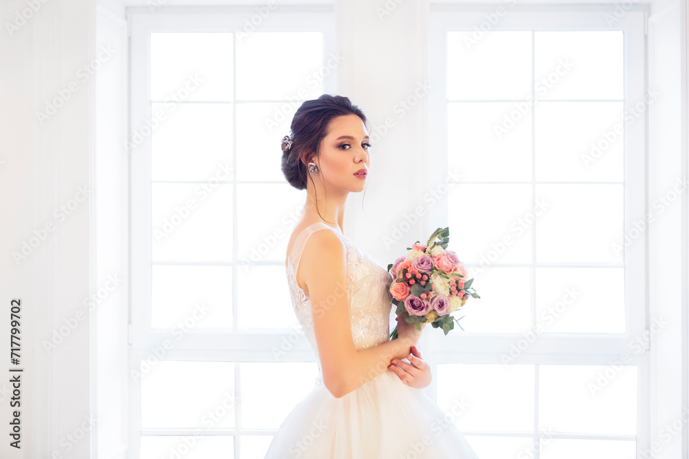 Beautiful brunette woman with bouquet posing in a wedding dress Beautiful brunette woman with bouquet posing in a wedding dress
