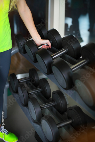 Young woman with barbells on gym background
