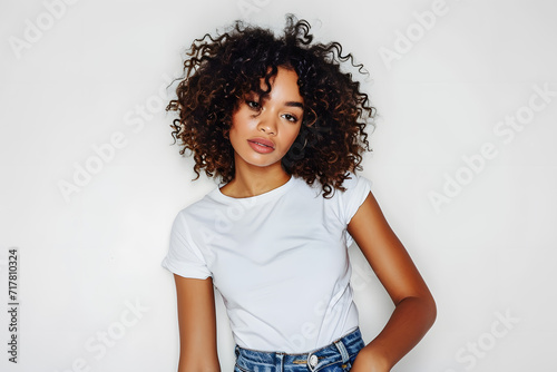 Young beautiful African American woman with curly hair in white t shirt posing with blue jeans isolated on light grey background