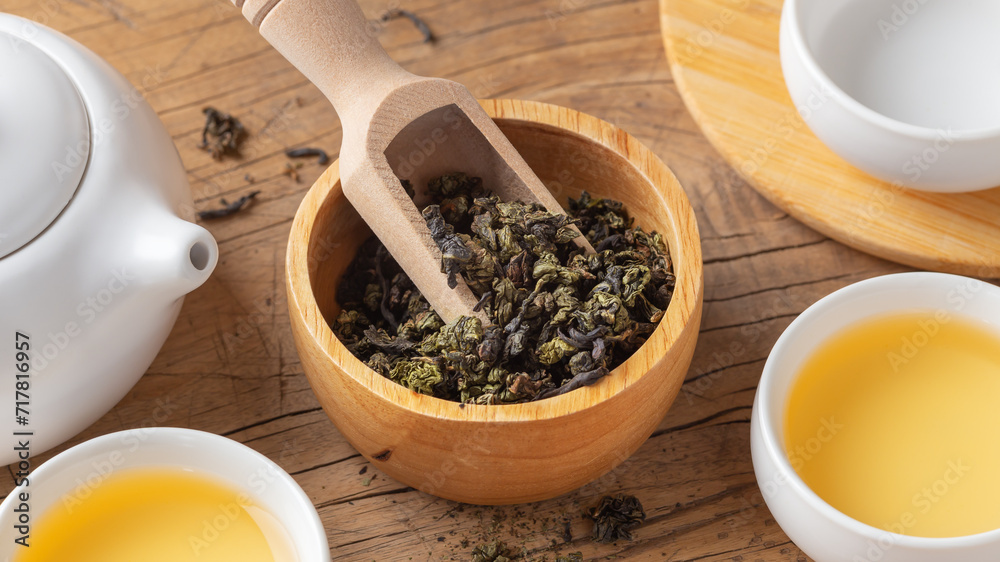 Dried tea leaves in wood bowl closeup with tea set on wooden table Dried tea leaves in wood bowl closeup with tea set on wooden table