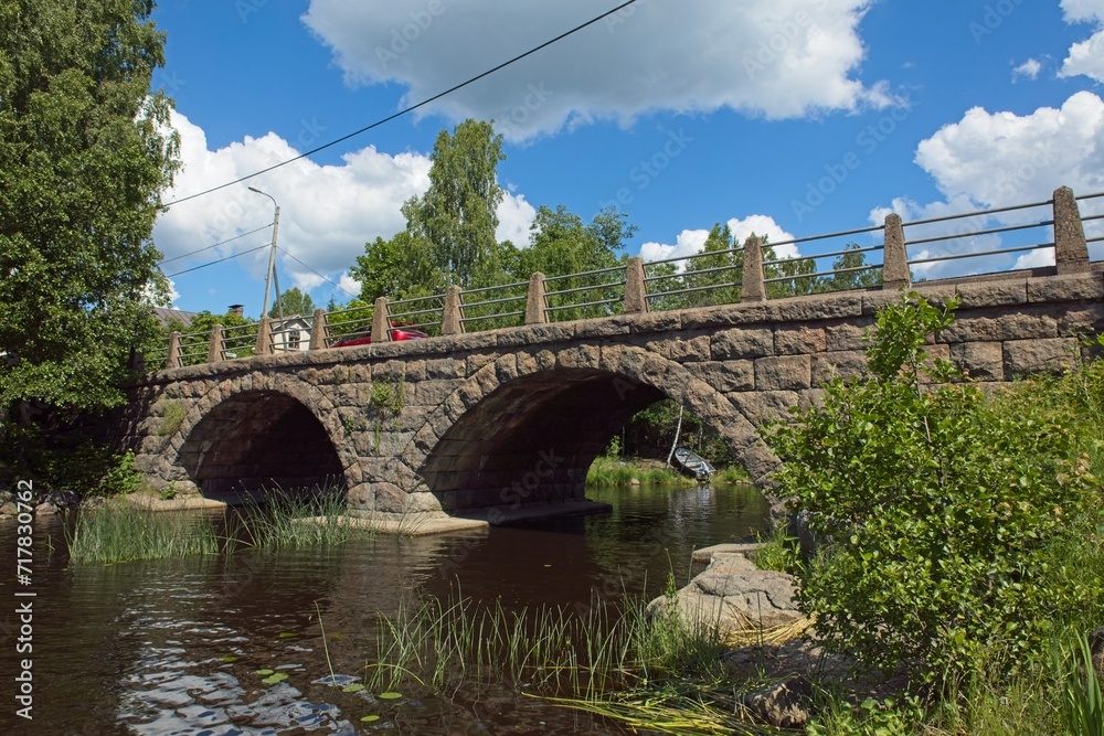 Self-supporting old stone bridge with arches over river in summer. Self-supporting old stone bridge with arches over river in summer.