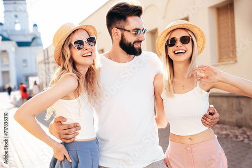 Group of young three stylish friends posing in the street. Fashion man and two cute female dressed in casual summer clothes. Smiling models having fun. Cheerful women and guy outdoors at sunny day