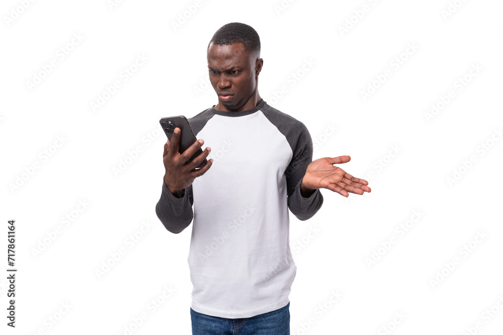 a young african guy with a short haircut wearing a long-sleeved summer sweater is indignant using a smartphone a young african guy with a short haircut wearing a long-sleeved summer sweater is indignant using a smartphone