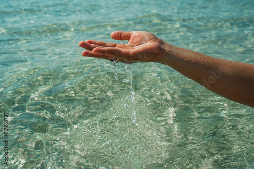 Tender touching surface of ocean water. Woman's hand touching surface of turquoise water in sunlight. Nature water concept, woman hand. Woman's hand at clear turquoise water. © SandyHappy