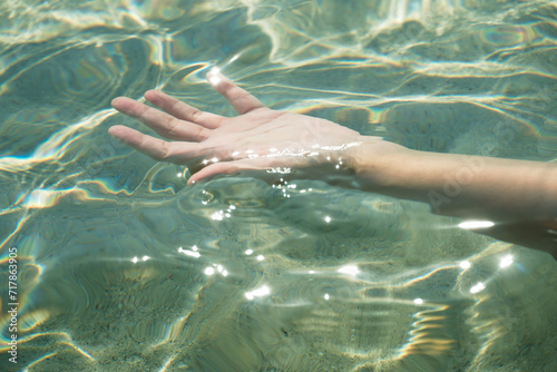Tender touching surface of ocean water. Woman's hand touching surface of turquoise water in sunlight. Nature water concept, woman hand. Woman's hand at clear turquoise water.