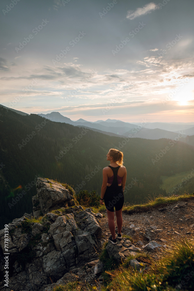 Rear view shot of young fit woman in stylish sportswear looking on the scenic view of mountains on beautiful sunset. Rysy mountains, Tatras. Poland, Slovakia