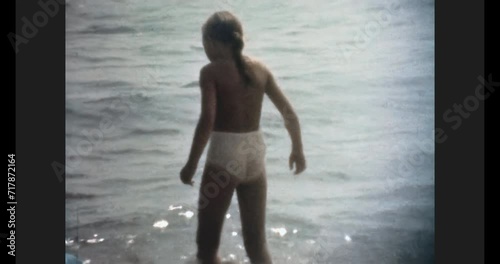 Little girl walk swimming in sea. Child walking along sandy beach in ocean waves. Happy kid in summer holidays at seaside. Carefree childhood. Vintage color film. Family archive. Retro vacation 1980s