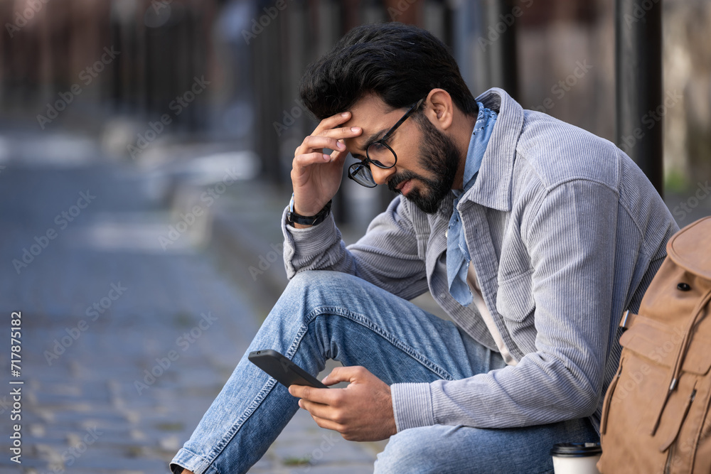 Dark-haired young man sitting on the pavement with a thoughtful look Dark-haired young man sitting on the pavement with a thoughtful look