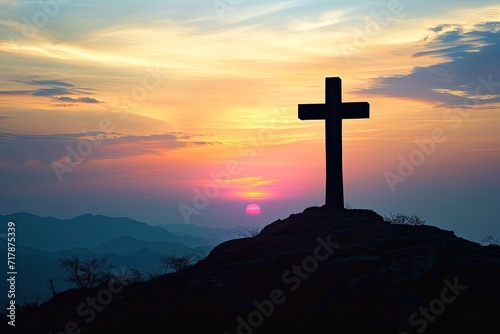 Silhouette of a cross on a hill in a mountain landscape at sunset.