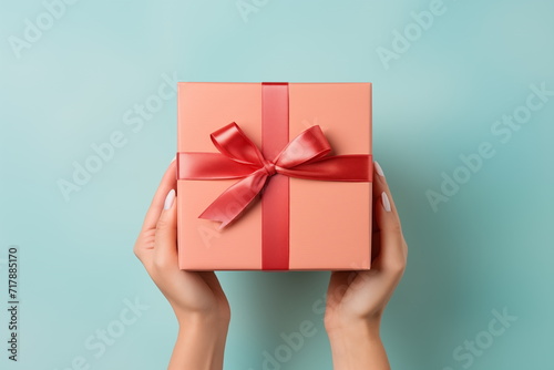 Top view of hands holding craft paper gift box with ribbon bow on isolated pastel blue background. Generated AI. photo