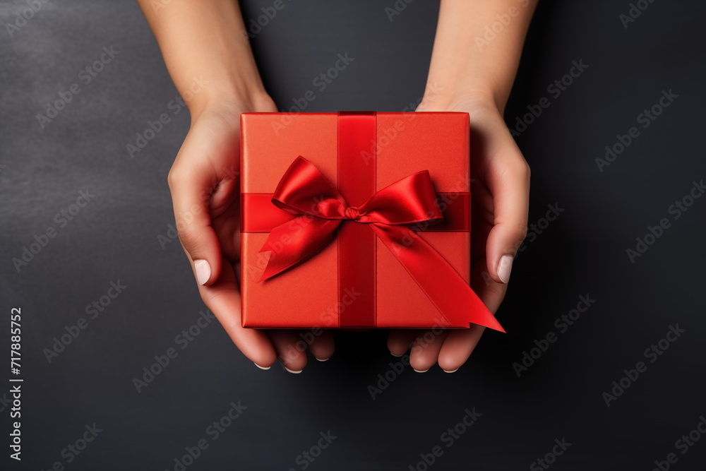 Top view of hands holding craft red paper gift box with ribbon bow on isolated black background. Generated AI. Top view of hands holding craft red paper gift box with ribbon bow on isolated black background. Generated AI.