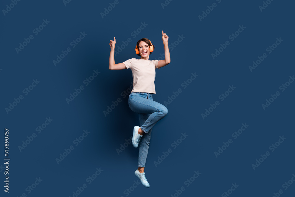 Full length photo of lovely young lady jump dancing headphones have fun wear trendy white garment isolated on dark blue color background