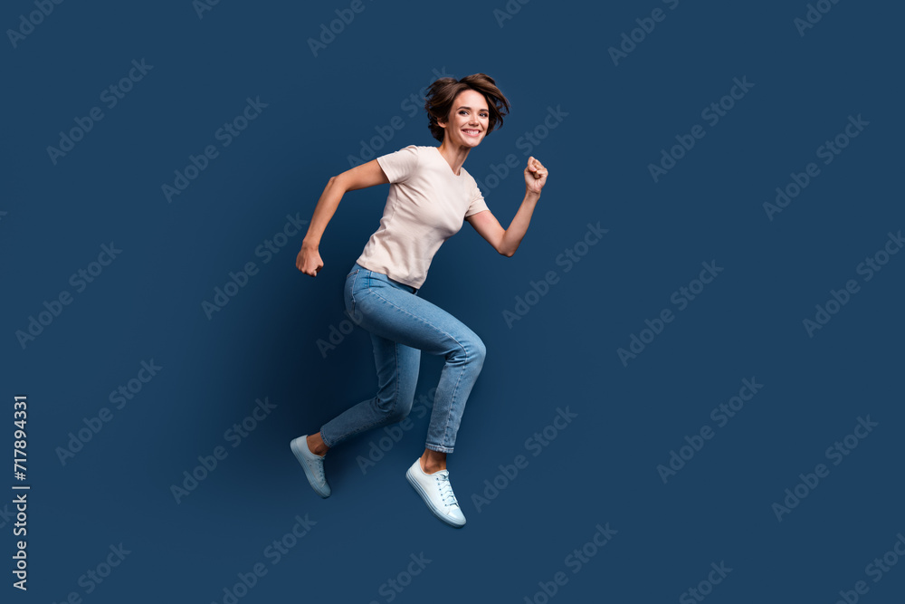 Full length photo of lovely young lady running hurry have fun shopping wear trendy white garment isolated on dark blue color background