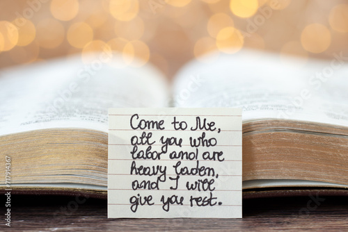Handwritten quote for Christians to come to God Jesus Christ's rest in front of an open holy bible book with bokeh light background. Close-up. Selective focus. Biblical concept. photo