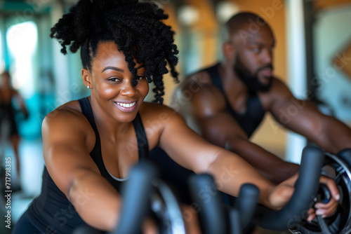 Young african american woman in gym, treadmill, in the background african american mandoing a spinning class at a gym