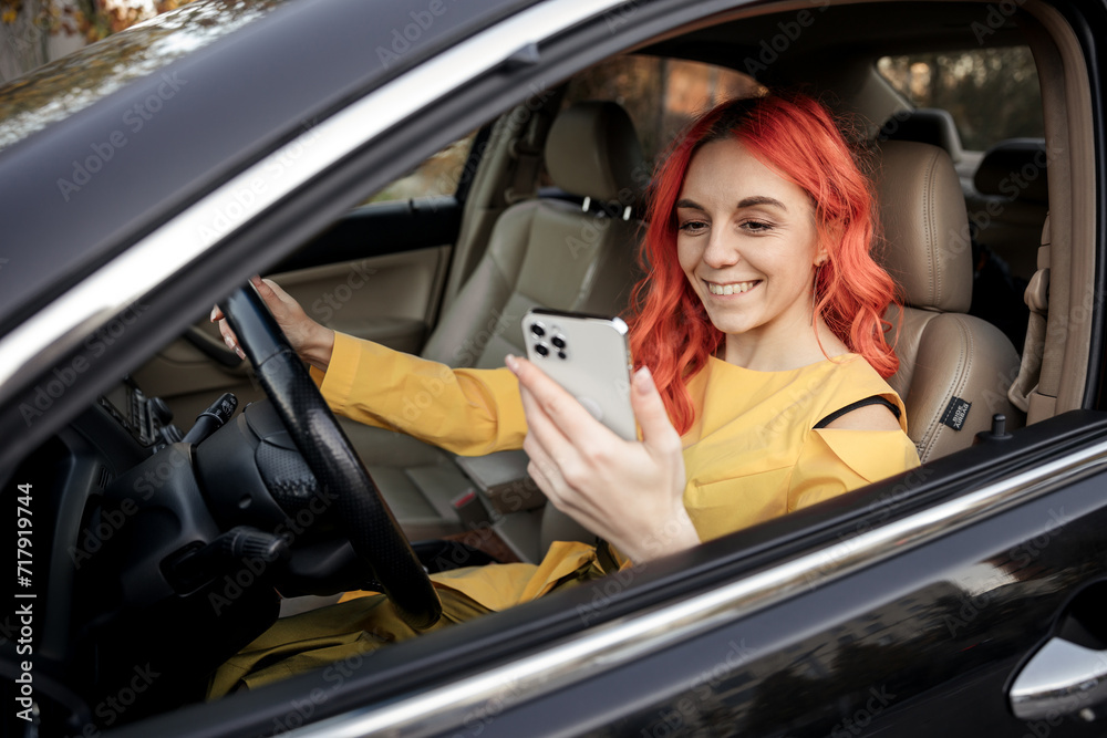 Car renting App. Happy young red head female look at smartphone while sitting inside of car. Car renting App. Happy young red head female look at smartphone while sitting inside of car.