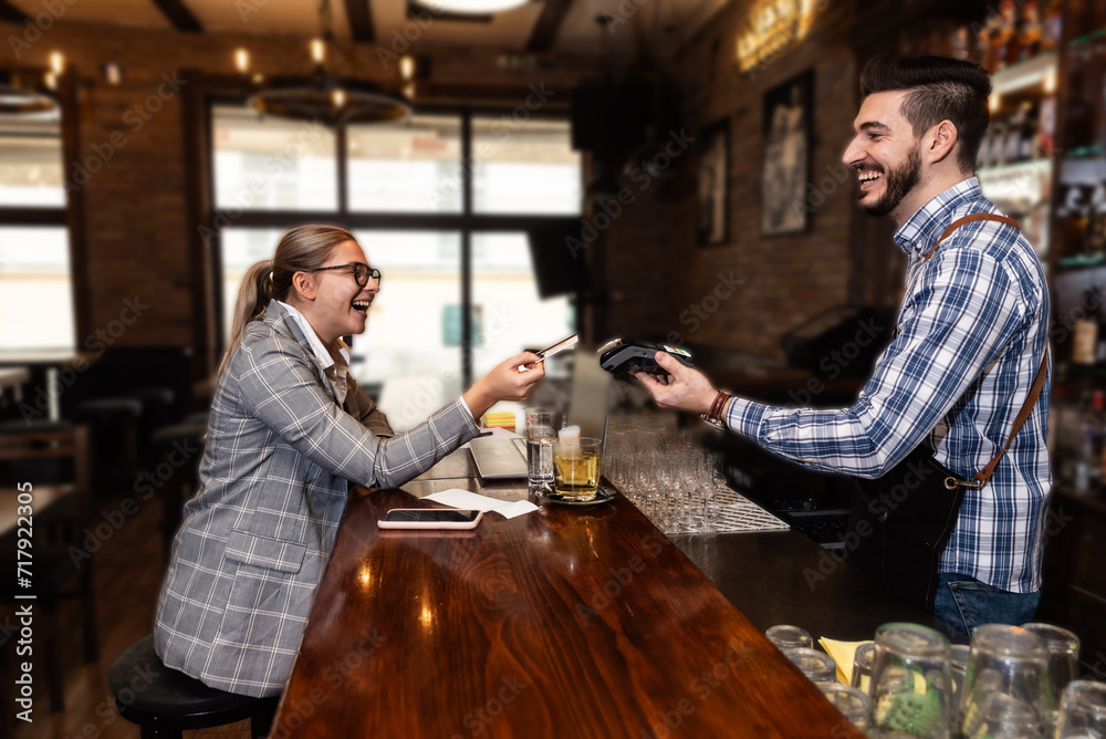 Business woman paying with a contactless debit credit card in a restaurant, waiter or barman holding a payment terminal. Transaction without contact, female pay for coffee or tea in coffee shop.