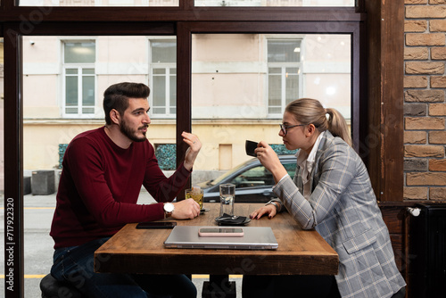 Young serious man having conversation with woman girlfriend sit at cafe table, focused male friend talking to female colleague client solving problem discuss work issues at meeting in coffeehouse photo