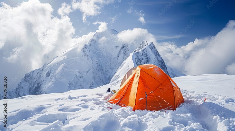 Mountaineer next to a striking orange tent on a snowy peak.