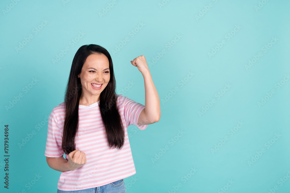 Fototapeta premium Photo of sweet lucky mixed race mestizo lady dressed striped t-shirt rising fists looking empty space isolated teal color background
