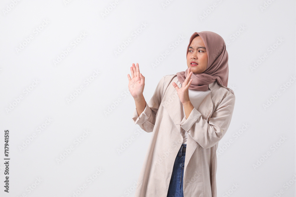 Portrait of attractive Asian hijab woman in casual suit forming a hand gesture to avoid something. Advertising concept. Isolated image on white background