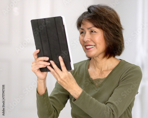 Happy attractive woman smiling enjoying looking at mobile tablet laughing talking using face time video chat white wall background.