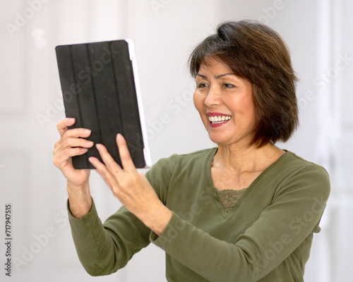 Happy attractive woman smiling enjoying looking at mobile tablet laughing talking using face time video chat white wall background.