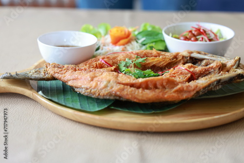 Deepfried sea bass with fish sauce served with mellow dipping sauce with sliced ​​mango to add flavor and fresh vegetables arranged in wooden plate. Deep-fried sea bass with fish sauce is popular dish