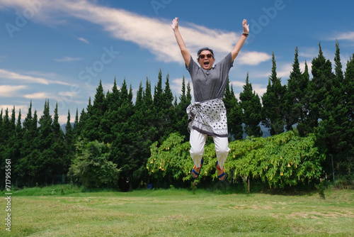 A woman wearing sunglasses is in the park, celebrating the sunny day by jumping as high as she can photo