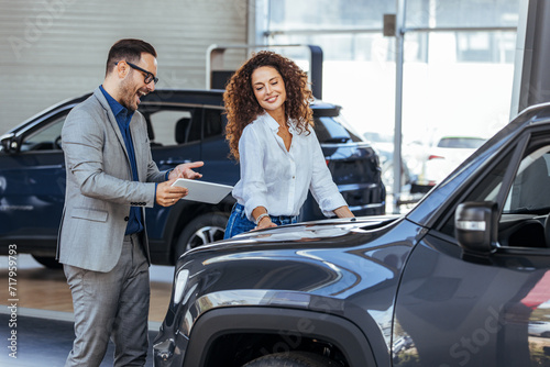 Woman in the showroom enjoying luxury car. Happy salesman selling the car to his female customer in a showroom. Auto business, car sale, consumerism and people concept