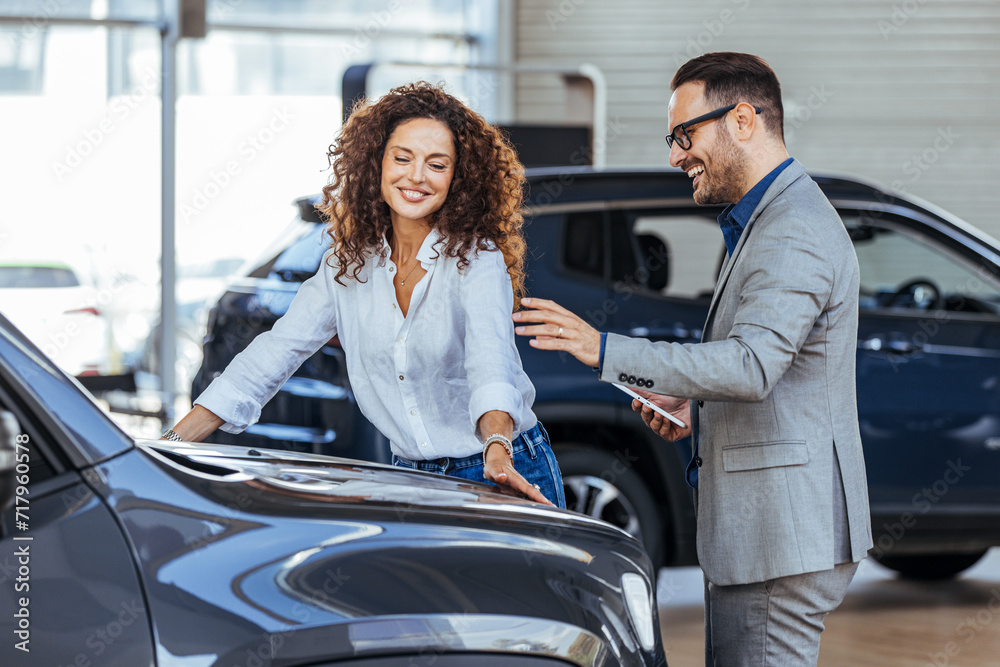 Woman in the showroom enjoying luxury car. Happy salesman selling the car to his female customer in a showroom. Auto business, car sale, consumerism and people concept Woman in the showroom enjoying luxury car. Happy salesman selling the car to his female customer in a showroom. Auto business, car sale, consumerism and people concept