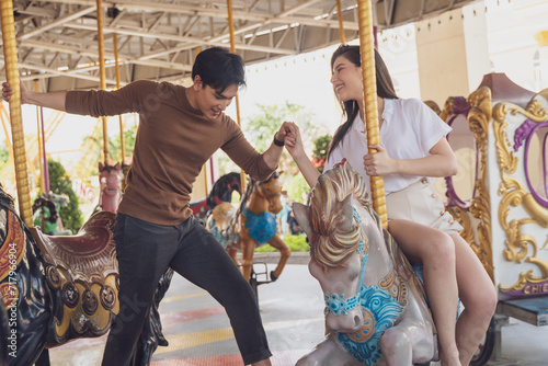 couple asian man and woman dating and riding on horse at Carousel amusement park. Concept happy and lovely life of teenager. photo