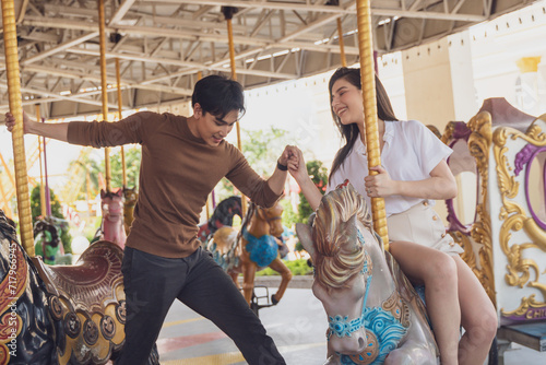 couple asian man and woman dating and riding on horse at Carousel amusement park. Concept happy and lovely life of teenager. photo