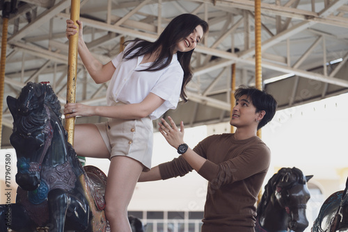 Young joyful couple man and woman riding on horse at Carousel amusement park. Concept happy and lovely life of teenager.