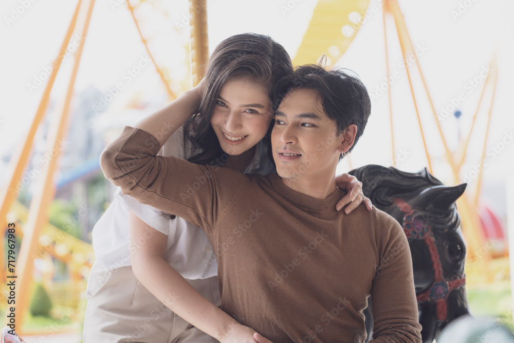 Obraz premium Young joyful couple man and woman riding on horse at Carousel amusement park. Concept happy and lovely life of teenager.