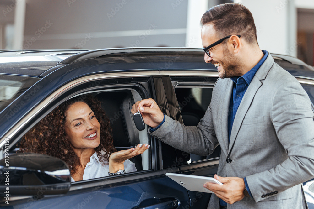 Car dealer giving key to new car owner. Happy woman taking the keys from the car dealer. Car dealer is giving key for a new car to a businesswoman