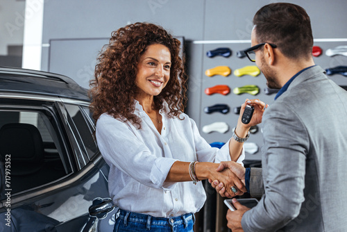 Smiling woman receiving her car keys in auto saloon. Happy salesman congratulating his female customer for buying a new car photo