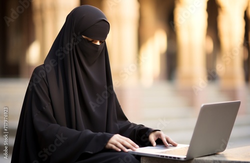 Middle Eastern woman wearing traditional robe using computer. Muslim entrepreneur performing tasks.