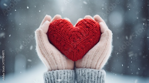 Female hands in knitted mittens with knitted heart on a snowy winter day.