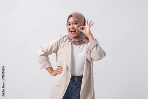 Portrait of excited Asian hijab woman in casual suit showing ok hand gesture and smiling looking at camera. Advertising concept. Isolated image on white background