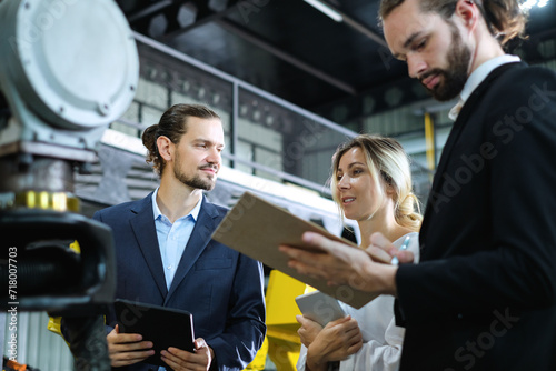 Bearded caucasian male engineer holding tablet talking with female engineer and teams about the problem of industrial robot arms in factory.