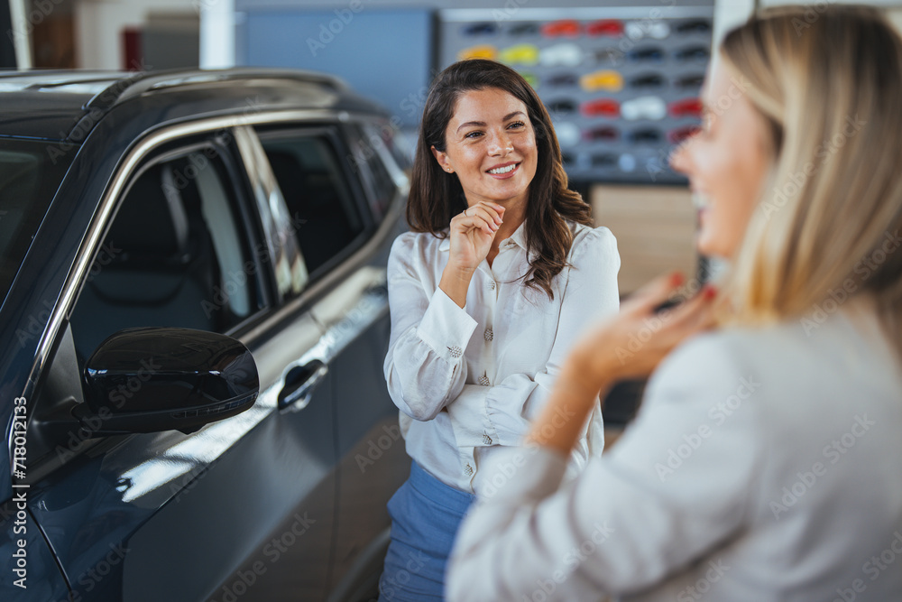 Businesswoman looking for a new car, standing next to a new SUV indoors at a car dealer. Beautiful young caucasian female client customer choosing new car, trying checking its options Businesswoman looking for a new car, standing next to a new SUV indoors at a car dealer. Beautiful young caucasian female client customer choosing new car, trying checking its options
