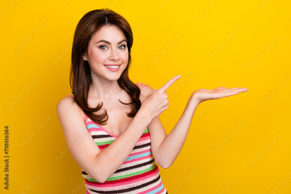 Photo of positive pleasant girl dressed striped top directing at offer on palm empty space isolated on vibrant yellow color background Photo of positive pleasant girl dressed striped top directing at offer on palm empty space isolated on vibrant yellow color background