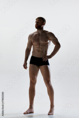 Full length portrait of young attractive man with perfect body shapes posing in underwear against white background. Concept of natural beauty, aesthetic of body, male health, masculinity.