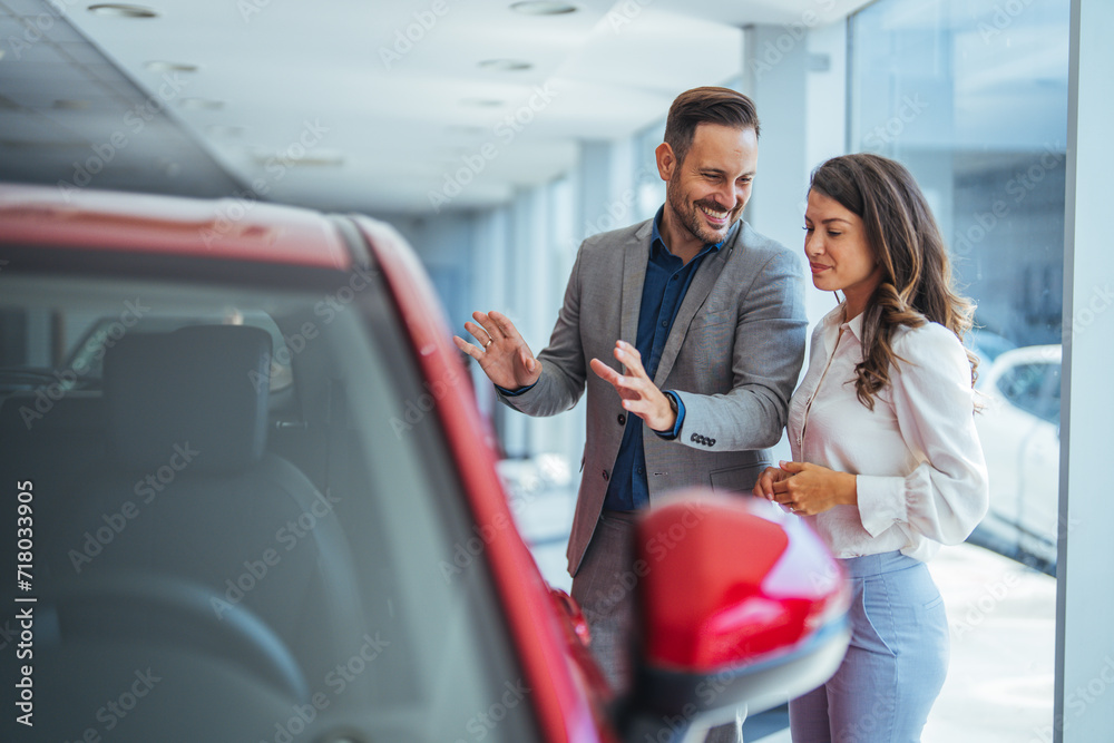 Happy couple communicating while searching for the right car in a showroom. Cute couple peering into a car at a dealer while deciding whether to buy Happy couple communicating while searching for the right car in a showroom. Cute couple peering into a car at a dealer while deciding whether to buy