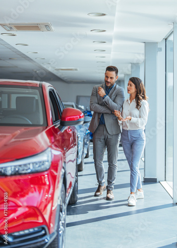 Young couple peering into a car at a dealer while deciding whether to buy it. Beautiful young couple choosing a new or used car at car showroom. Couple hugging and smiling at new car showroom © Dragana Gordic