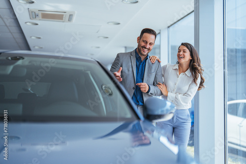 Happy couple communicating while searching for the right car in a showroom. Cute couple peering into a car at a dealer while deciding whether to buy