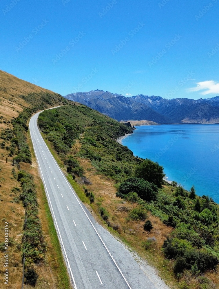 Aerial view of a road on the shore of Lake Hawea surrounded by lush greenery. New Zealand