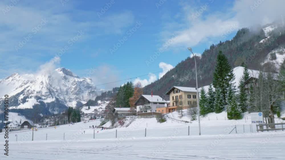A magnificent mountain ridge covered in snow is seen on a panoramic view together with mountain chalets and houses of local citizens, Engelberg, Switzerland A magnificent mountain ridge covered in snow is seen on a panoramic view together with mountain chalets and houses of local citizens, Engelberg, Switzerland